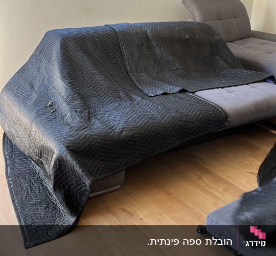 שמיכה שחורה מכסה ספה בחדר עם רצפת עץ